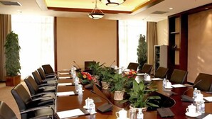 Un salón de conferencias con una mesa larga, sillas y plantas en macetas.