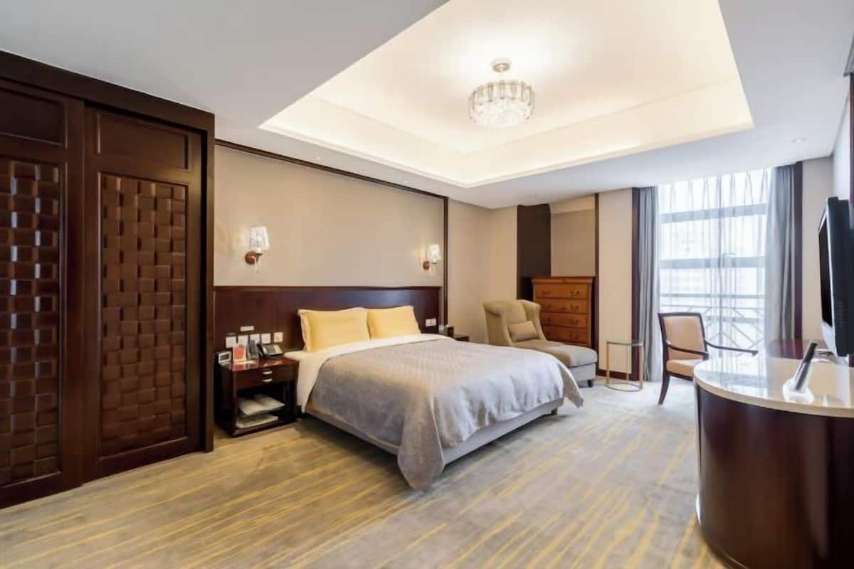 A hotel room with a bed, a desk, a chair, a TV, and a chandelier.
