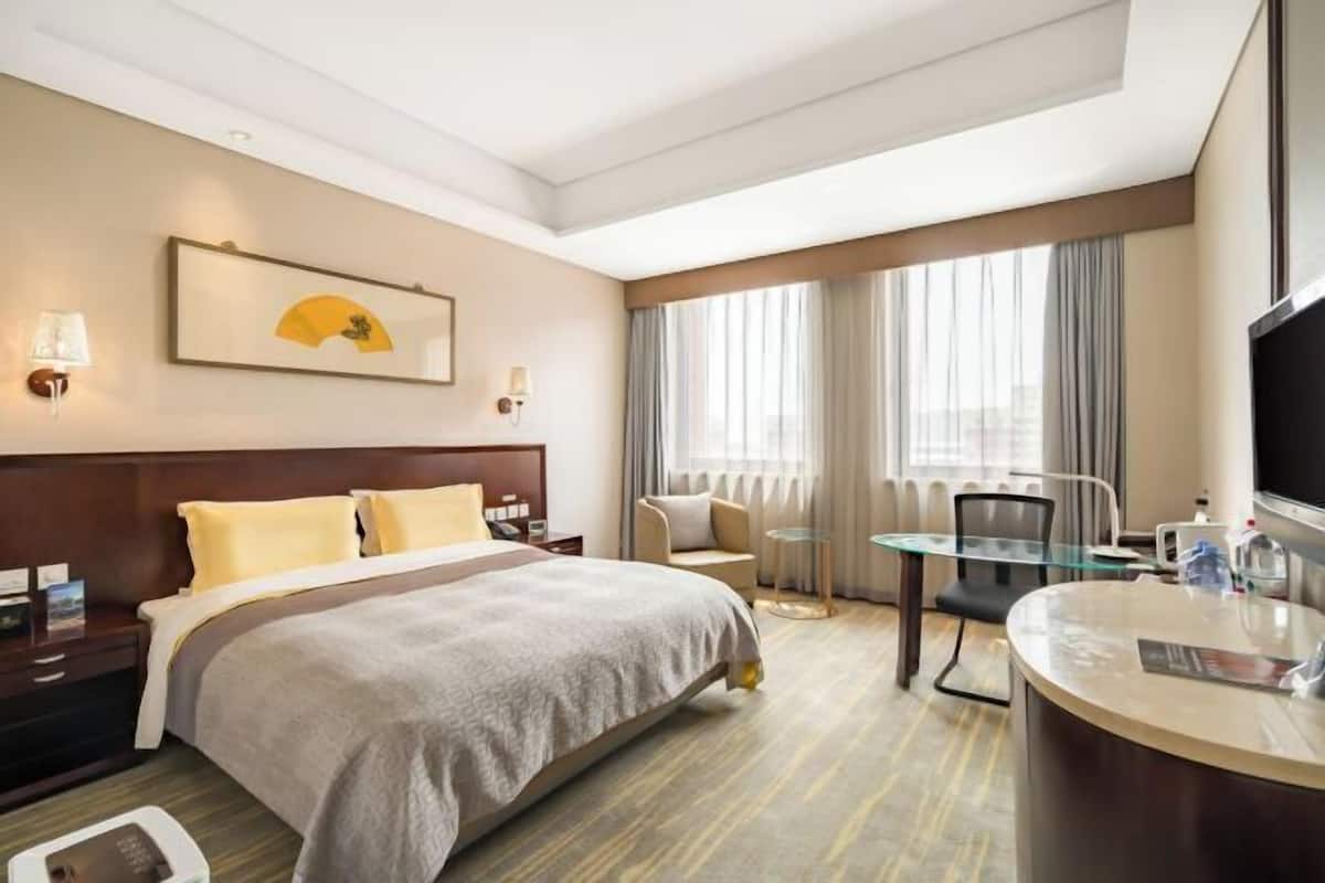 A hotel room with a bed, bedside tables, a desk with a chair, a television, and a window with curtains.