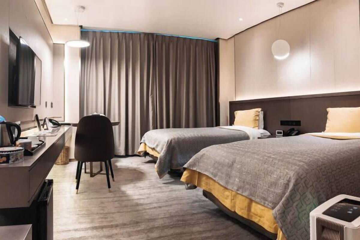 A hotel room with two beds, a desk, a chair, a TV, and a large window with curtains.