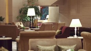 A hotel lobby with multiple sofas and armchairs arranged in a semi-circle, a large potted plant, and a painting on the wall. - Beijing International Cultural Exchange Center (Beijing)