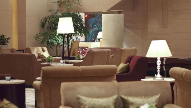 Un vestíbulo de hotel con varios sofás y sillones dispuestos en semicírculo, una planta grande en maceta y un cuadro en la pared.