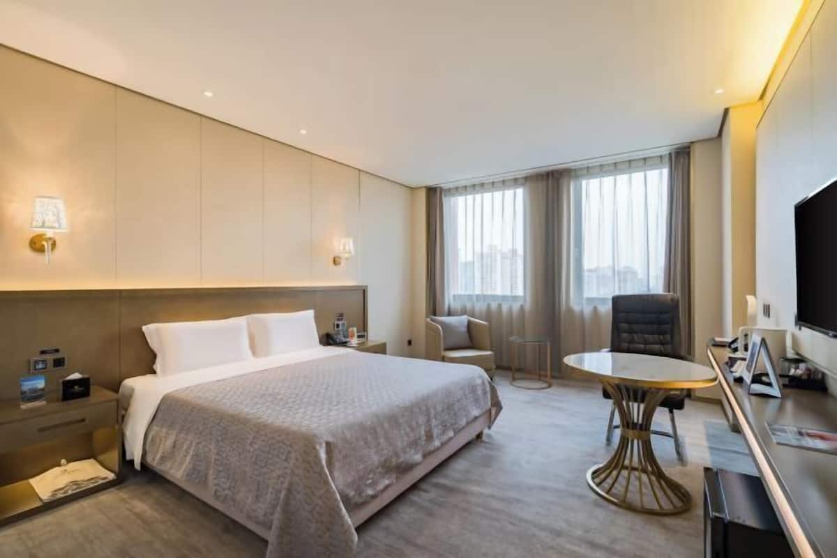 A hotel room with a large bed, a desk with a chair, a TV, and a window with curtains.