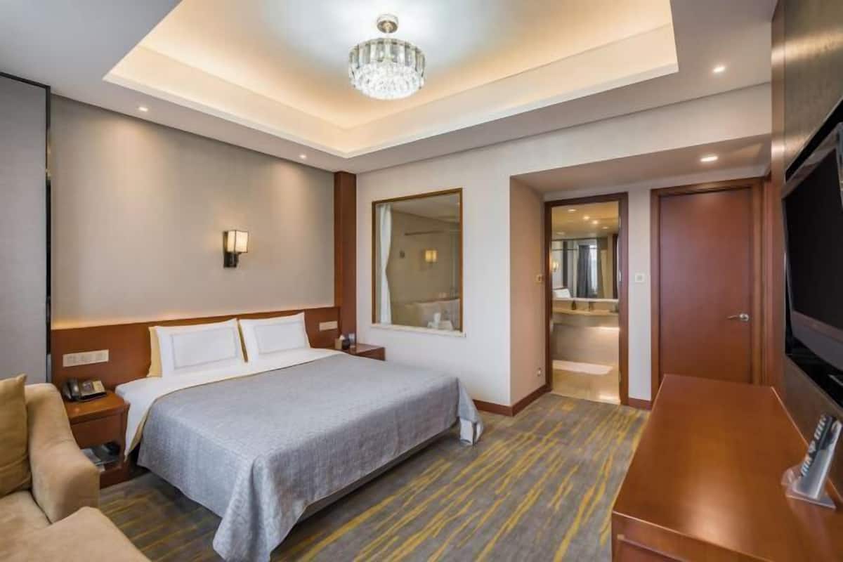 A hotel room with a bed, a desk, a TV, a chandelier, and a mirror.