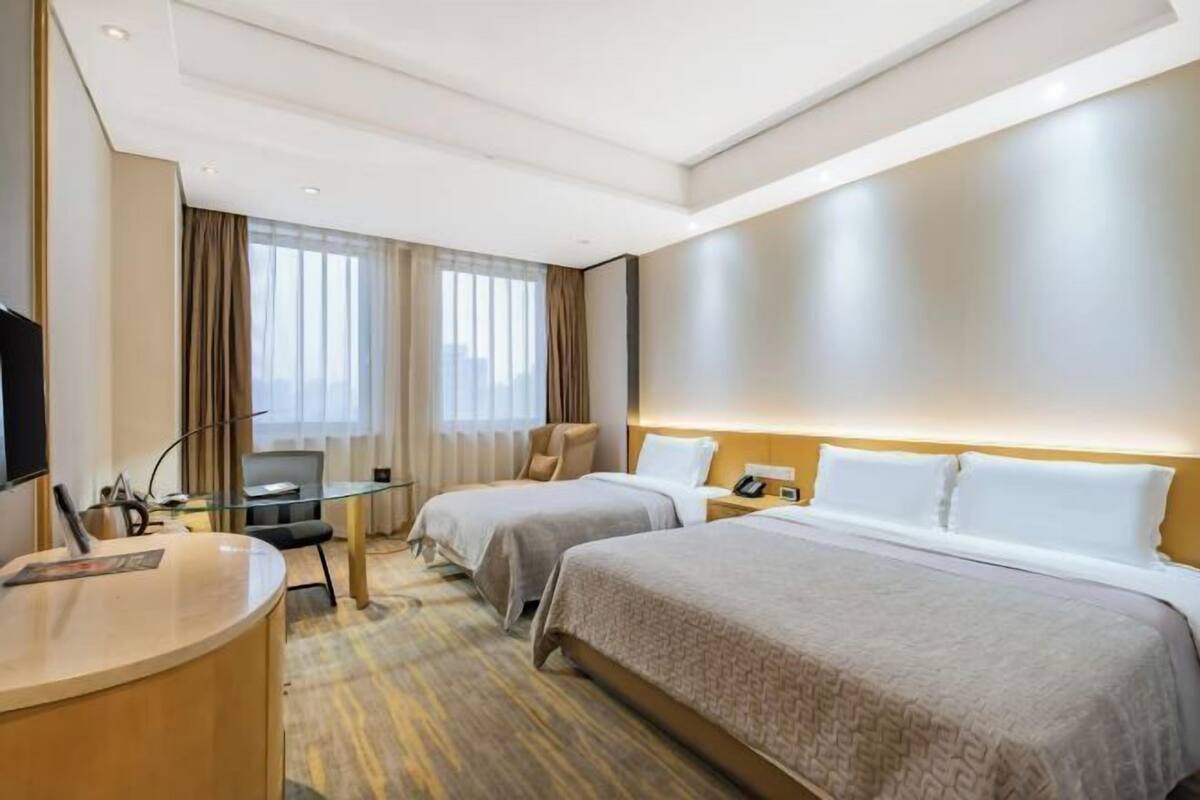 A hotel room with two beds, a desk, a chair, and a television.