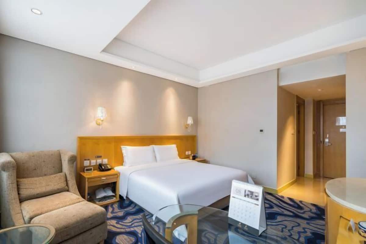 A hotel room with a bed, a chair, a desk with a calendar, and a nightstand.