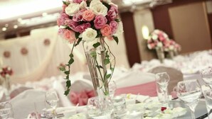 Un salón de banquetes con mesas dispuestas para un evento formal, con centros de mesa florales y cristalería.