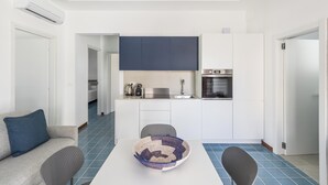 A modern kitchen with white cabinets, a blue backsplash, and a dining area with a white table and two chairs. - 4019 Villetta Biancamare by Barbarhouse (Carovigno)