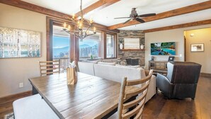 A dining area with a wooden table, chairs, a chandelier, and a view through large windows. - Close to Skiing and Winter Sports, Gas Log Fireplace, Mtn View, Gated Resort, In (Boone)