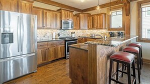 A kitchen with wooden cabinets, stainless steel appliances, a granite countertop, and a large island with stools. - Close to Skiing and Winter Sports, Gas Log Fireplace, Mtn View, Gated Resort, In (Boone)
