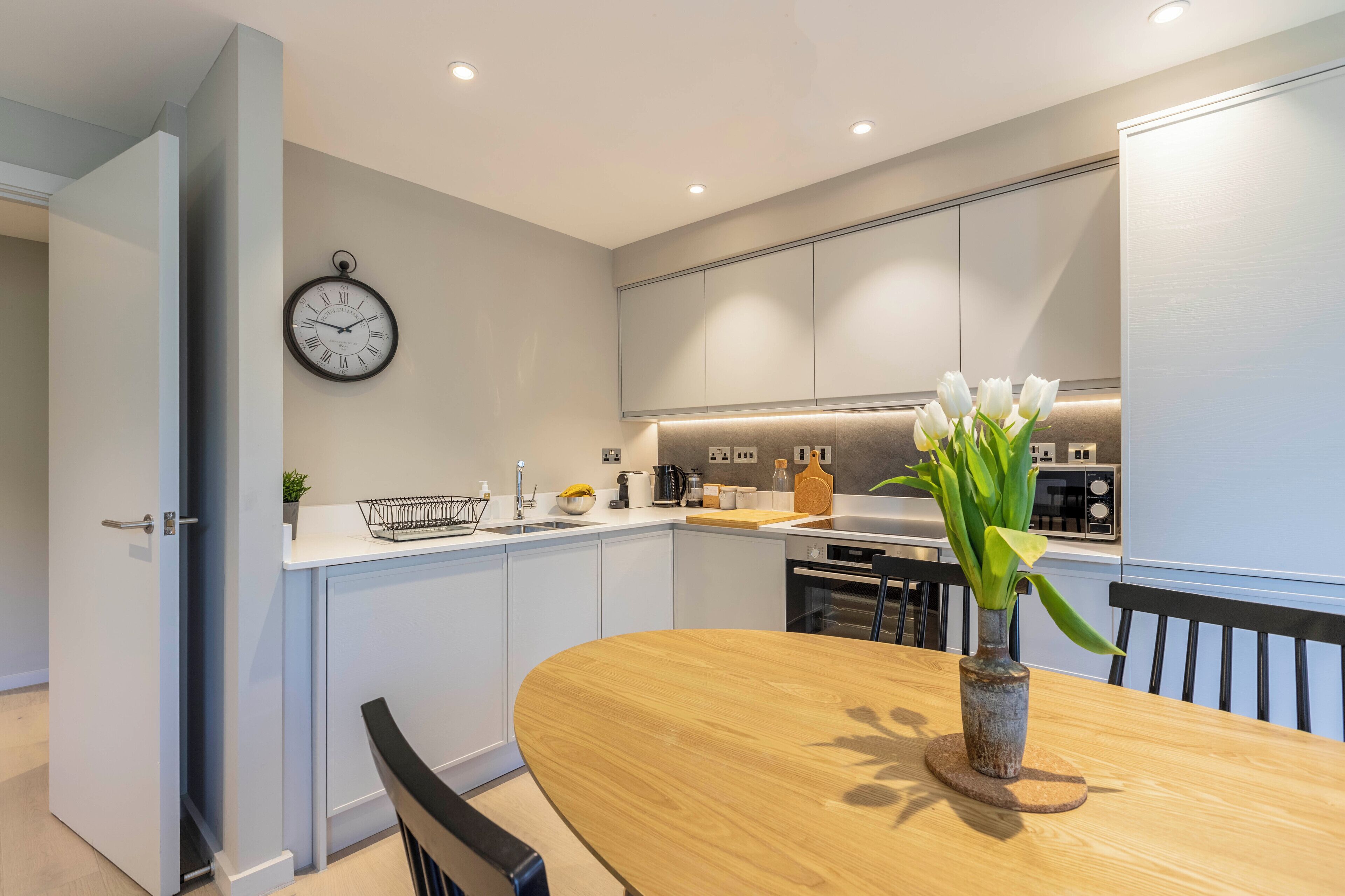 Una cocina moderna con una mesa de comedor de madera, un reloj en la pared y un jarrón con flores.