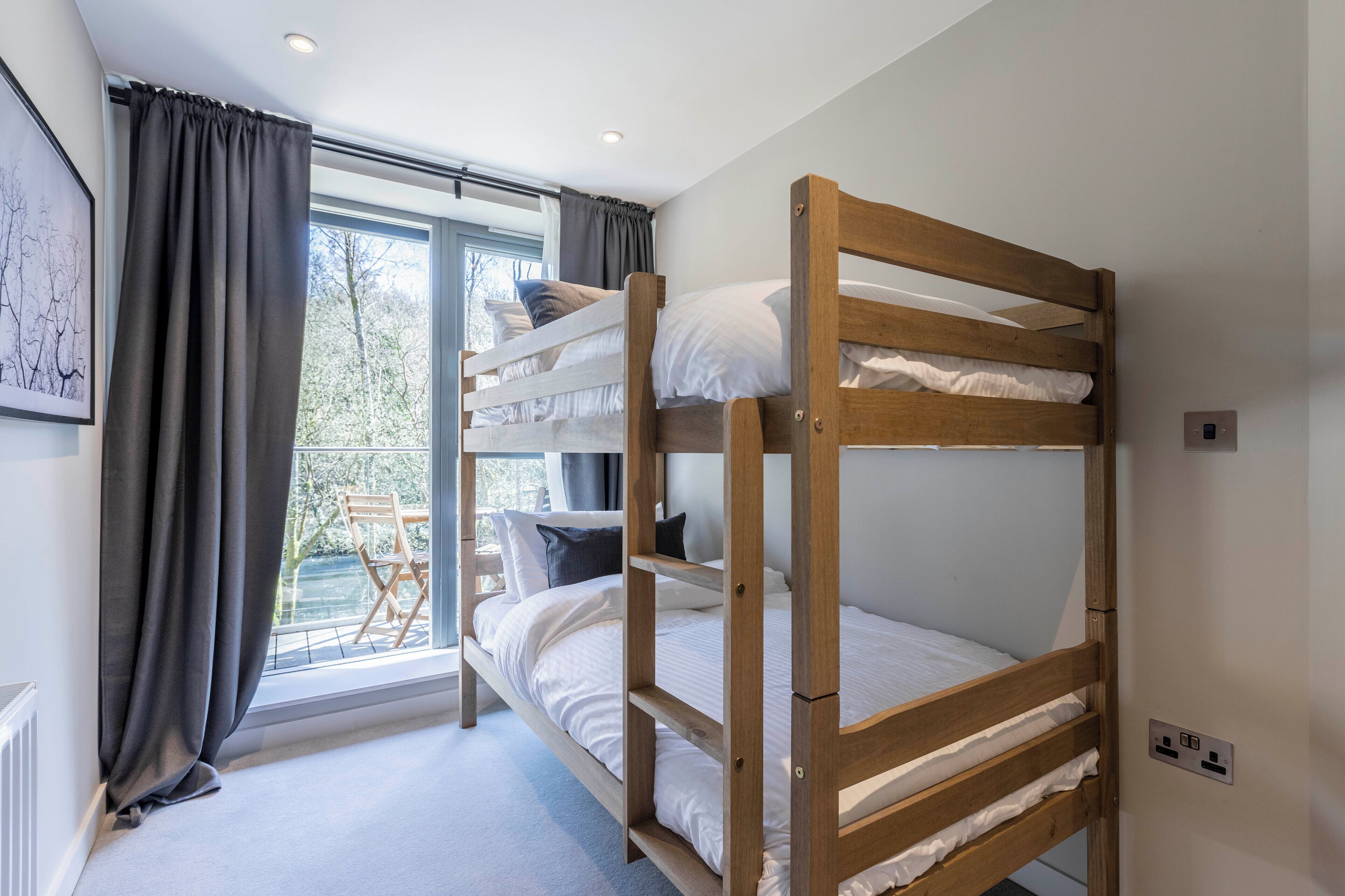 A bunk bed room with a view of trees through a window, a radiator, and a power outlet on the wall.