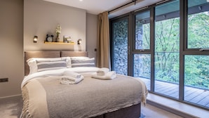 Quarto moderno com uma cama grande, parede de pedra e vista para o verde através de janelas amplas.