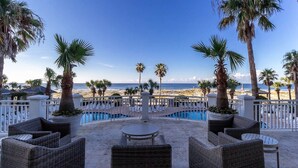 Un espace aménagé au bord de la piscine, avec des meubles en osier, une vue sur la plage et des palmiers.