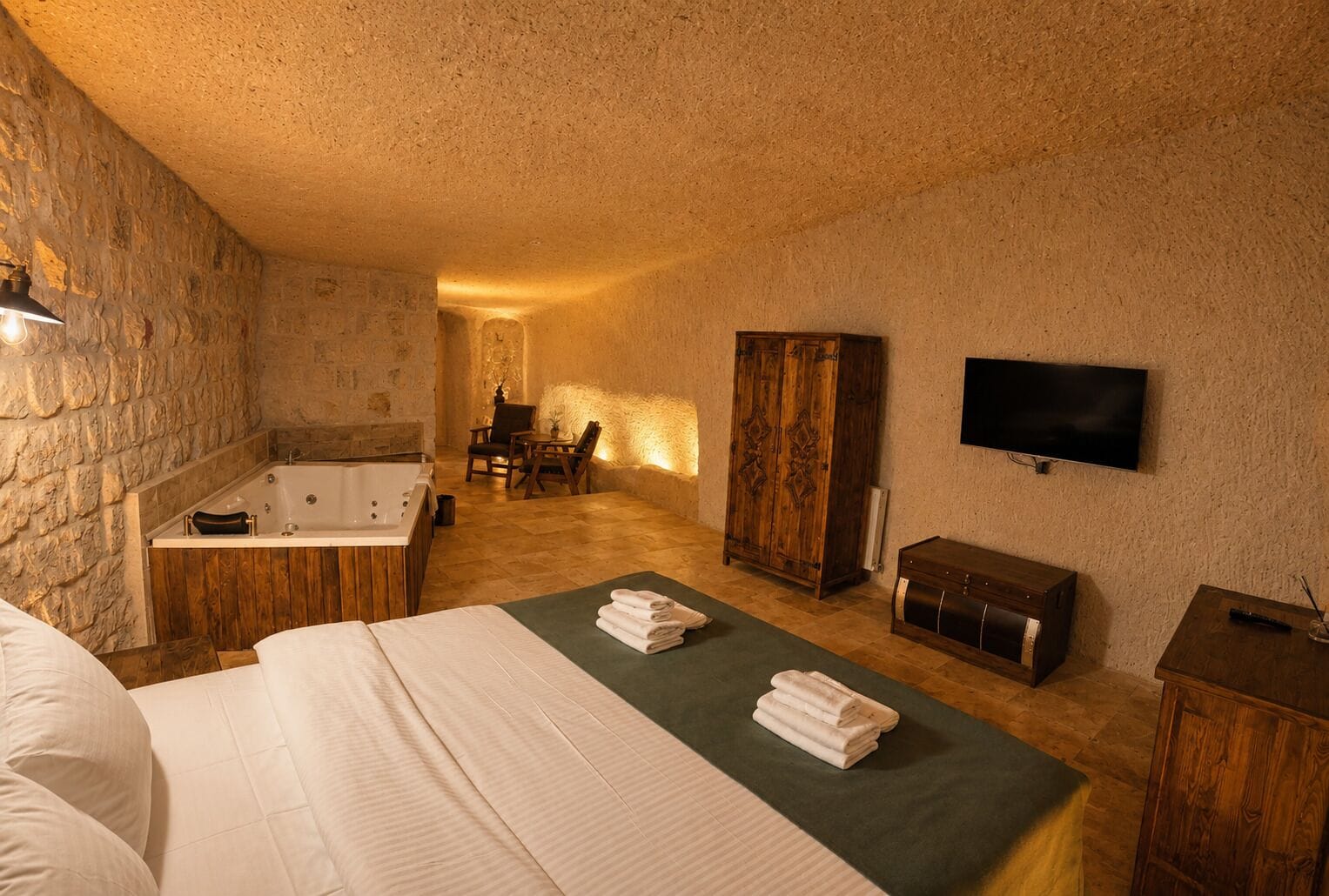A bedroom with a large bed, a bathtub, a wooden wardrobe, and a television.