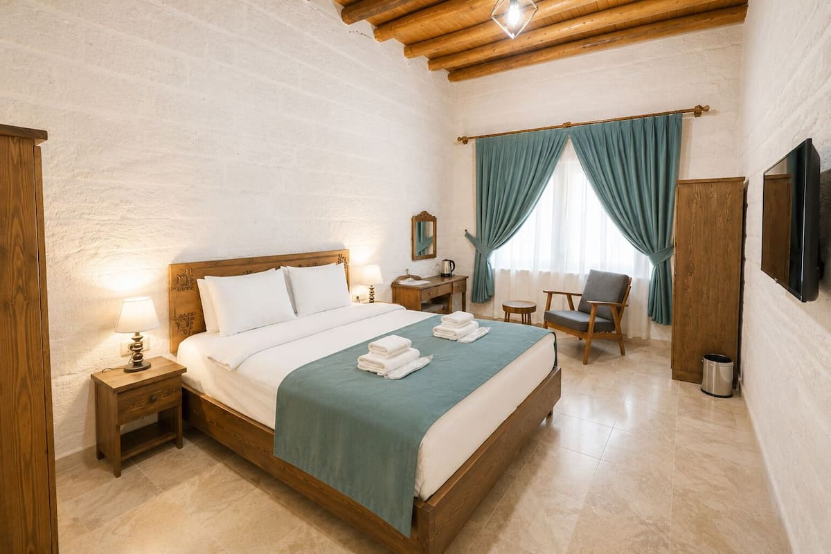 A hotel room with a wooden bed, a desk, a chair, a TV, and a mirror.