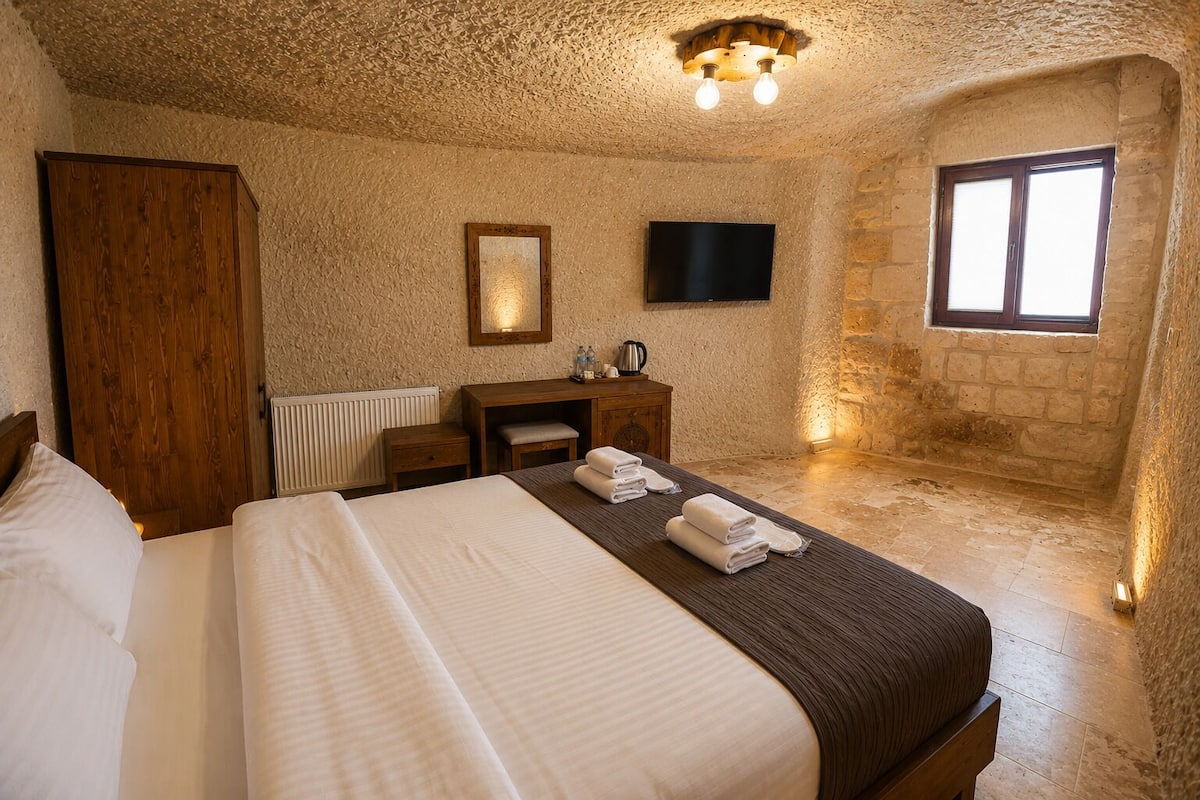 A bedroom with a bed, a wooden desk, a television, and a stone wall.