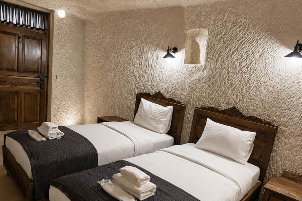 A room with two wooden beds, a wooden wardrobe, a small table, and a wall-mounted light fixture.