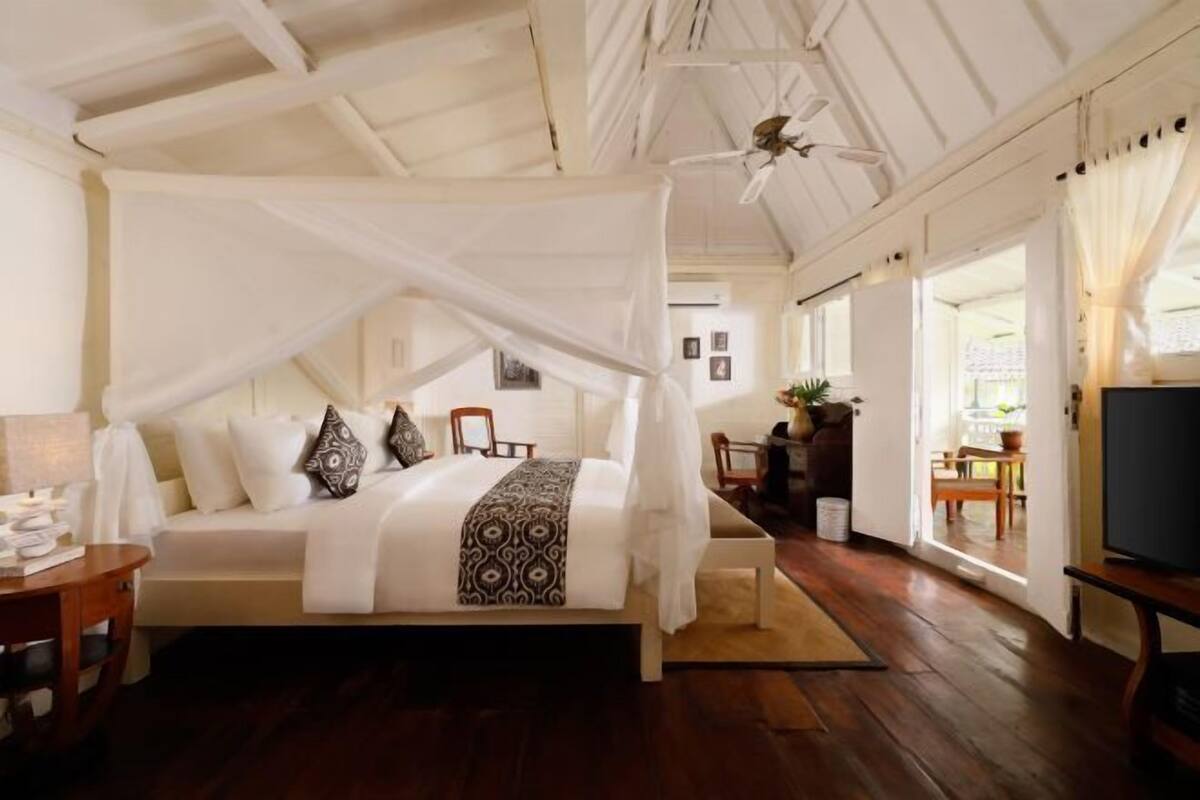 Een slaapkamer met een hemelbed, een houten vloer, een televisie en uitzicht op buiten.