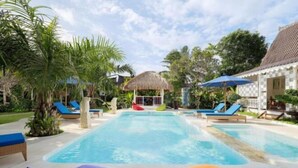 A pool area with lounge chairs and umbrellas, surrounded by palm trees and a thatched-roof structure. - Puri Tempo Doeloe Boutique Hotel (Bali)