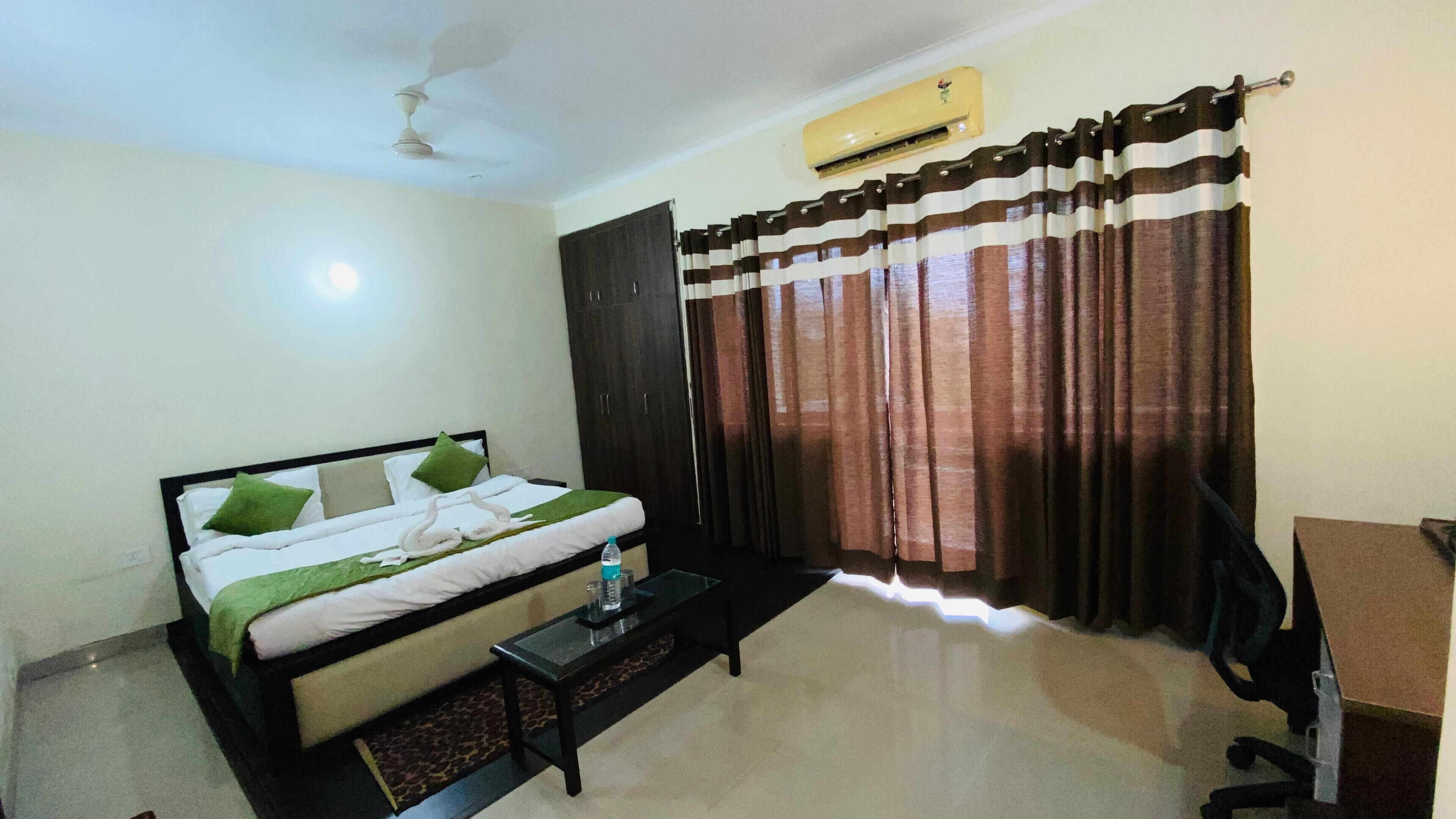 Una habitación de hotel con cama, una mesita, una silla, un armario y una ventana con cortinas.