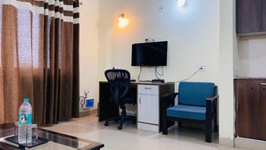 A small, tidy room with a desk, chair, and a television mounted on the wall. - LivBox Rudrapur (Kichha)