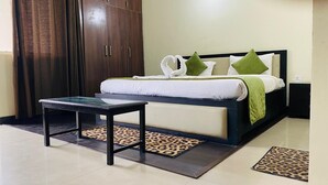 A hotel room with a bed, a nightstand, a table, and a wardrobe. - LivBox Rudrapur (Kichha)