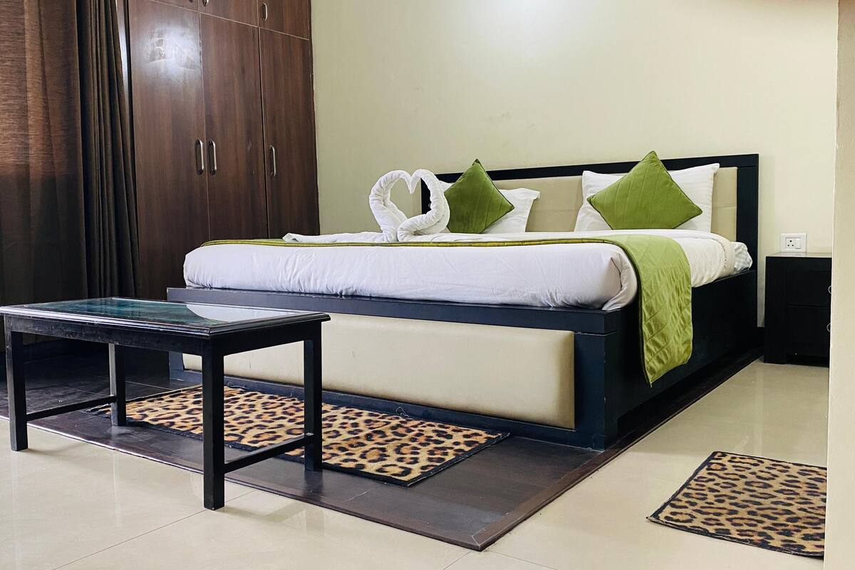 A hotel room with a bed, a nightstand, a table, and a wardrobe.
