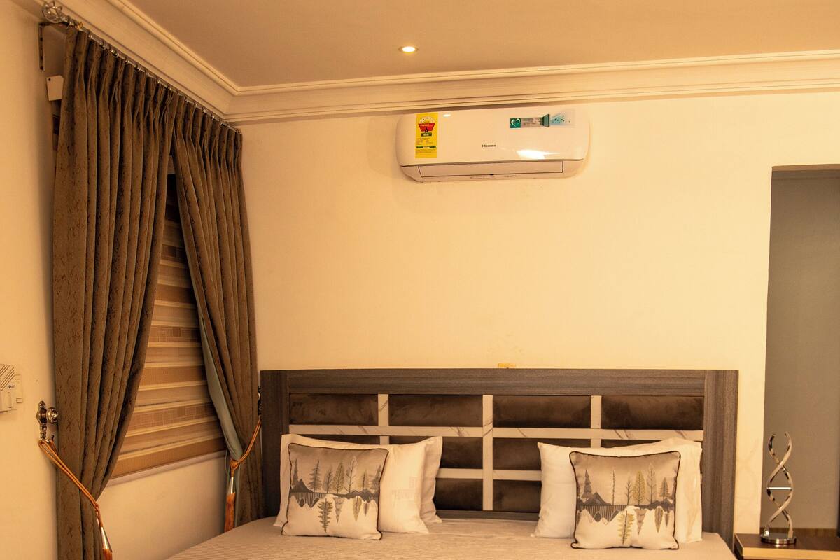 Een net opgemaakt bed met hoofdeinde, nachtkastje en een wandairconditioner.