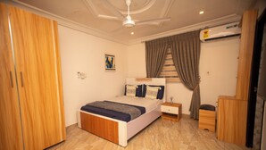 A bedroom with a bed, wardrobe, bedside table, and an air conditioning unit. - Lily Of De Valley Residence (Kumasi)