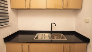 A small kitchen with a black countertop, a stainless steel sink, and beige cabinets. - Lily Of De Valley Residence (Kumasi)