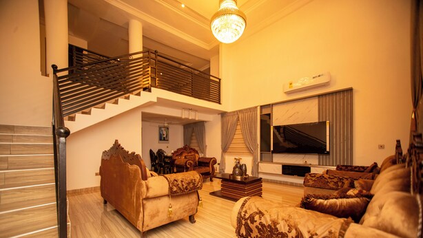 A spacious living room with a staircase, a chandelier, a flat-screen TV, and classic furniture. - Lily Of De Valley Residence (Kumasi)