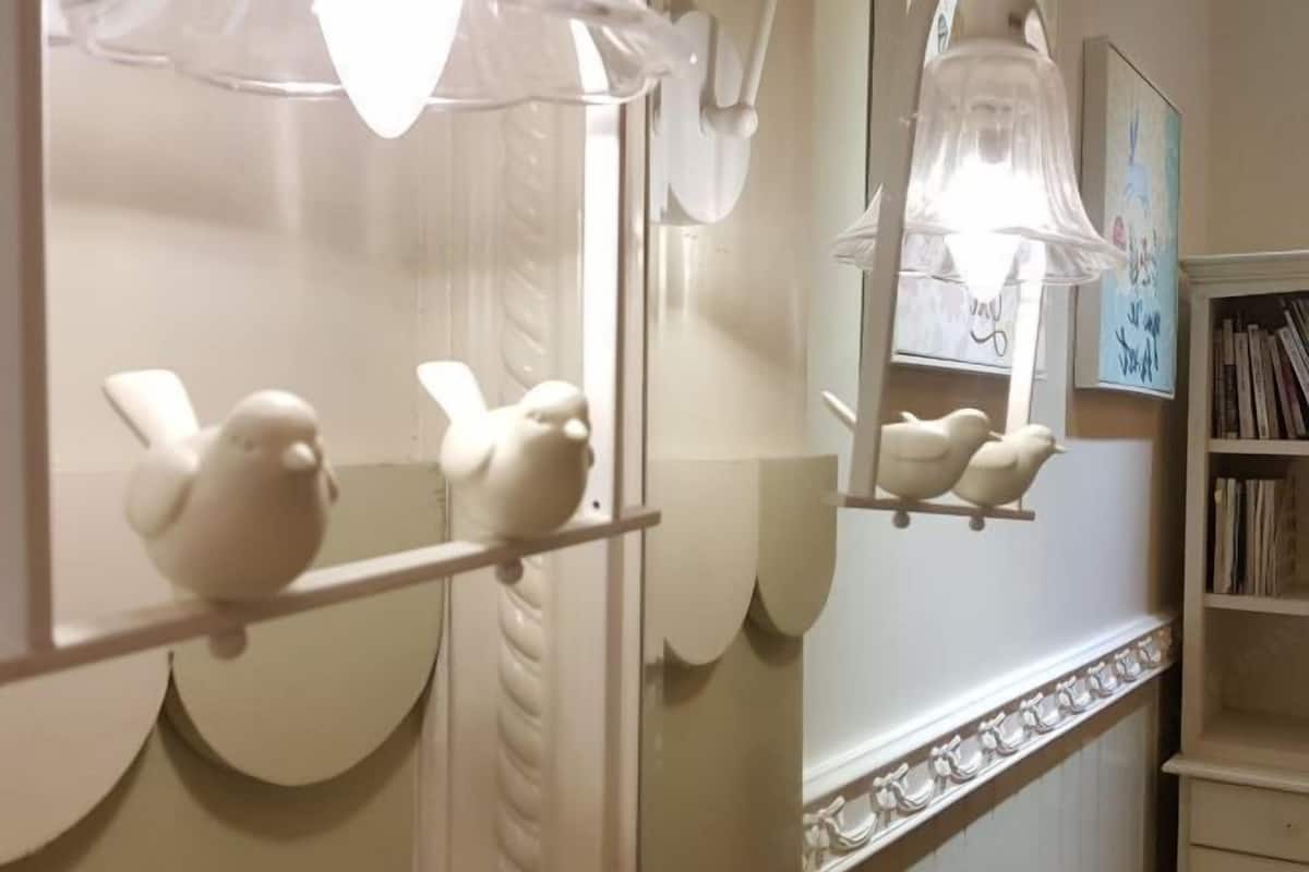 Un baño con sanitarios blancos, un espejo y una repisa con dispensadores de jabón con forma de pájaro.