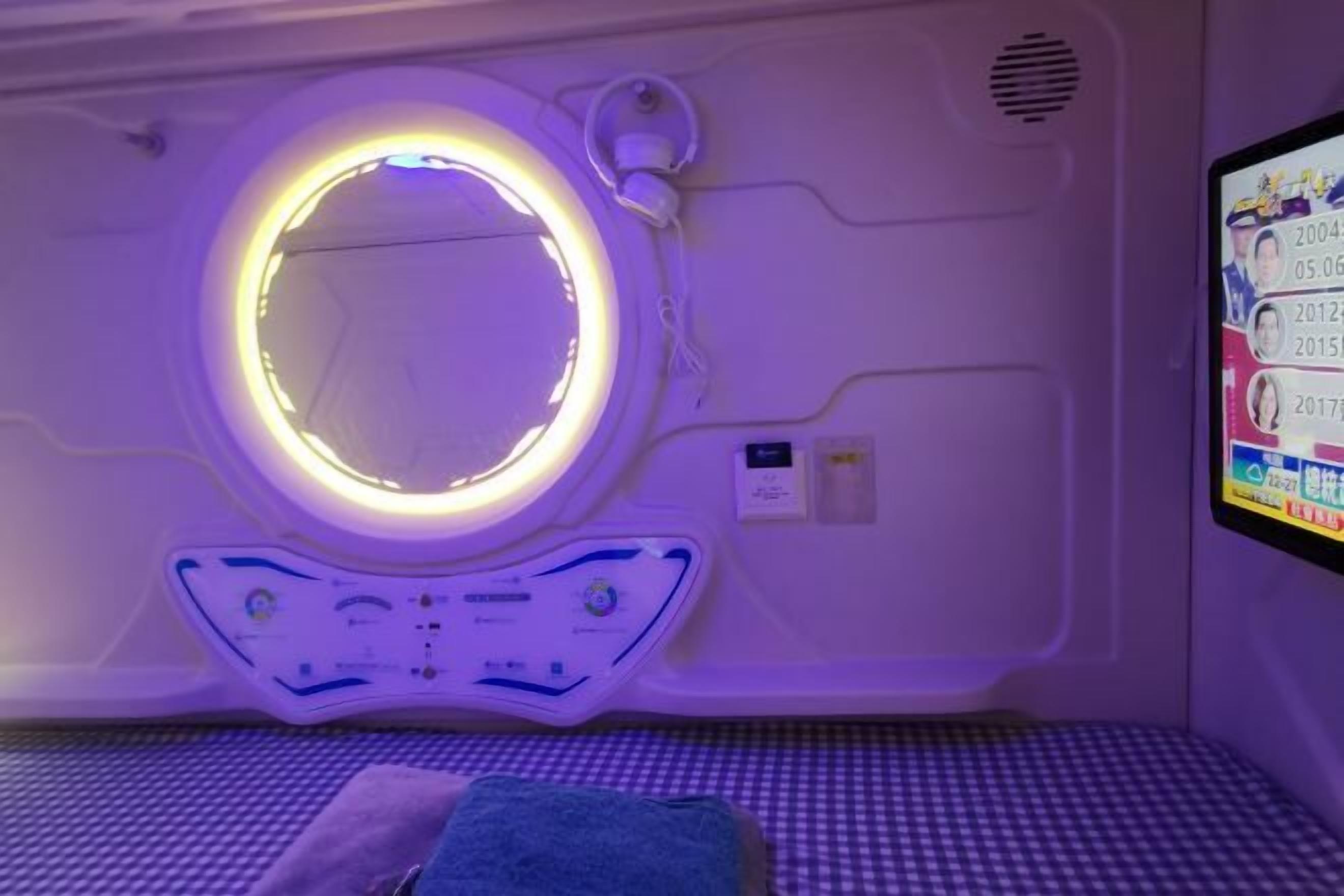 Quarto com luminária circular, painel de controle e tela digital na parede.
