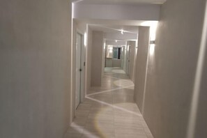 A long, narrow hallway with white walls and a light-colored floor, leading to a room with a window and a door. - TW Hostel 2 (Taipei)