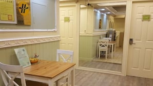 Un pasillo de hotel con una mesa y sillas de madera, un espejo que refleja la habitación y una puerta con un letrero.