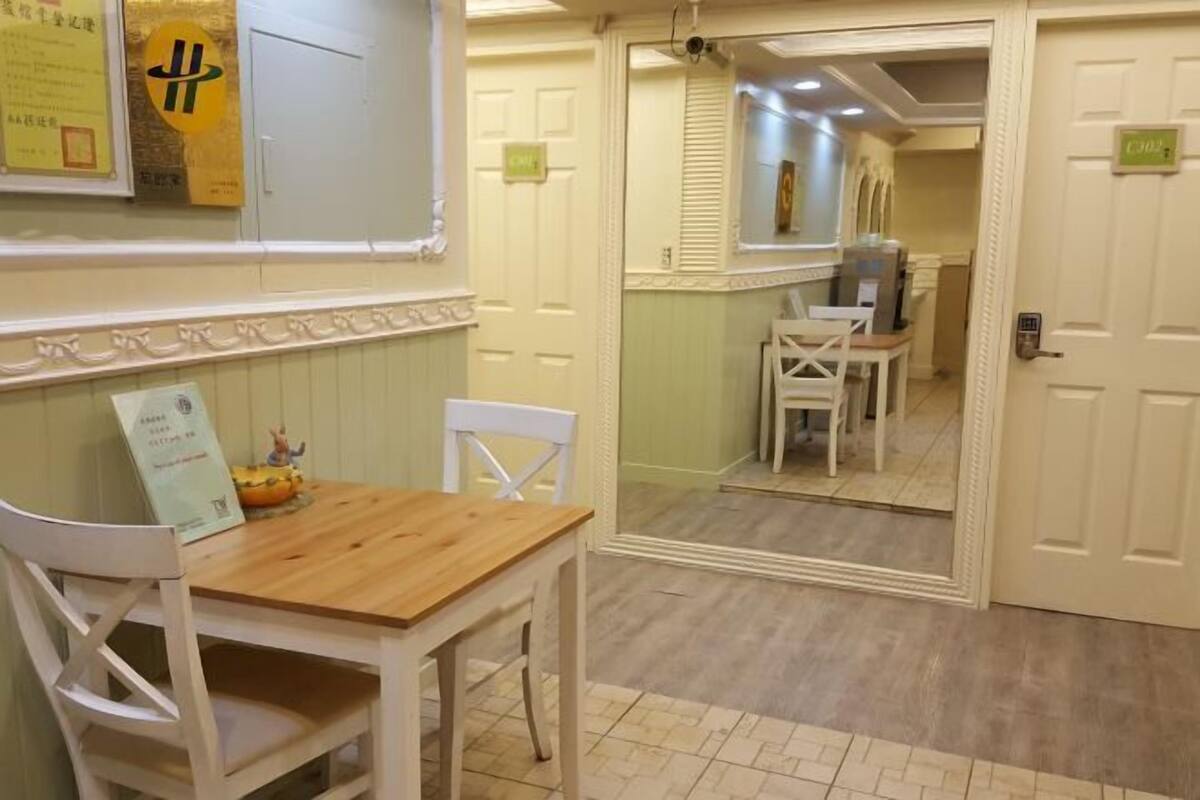 Un pasillo de hotel con una mesa y sillas de madera, un espejo que refleja la habitación y una puerta con un letrero.
