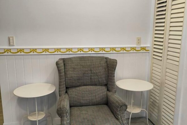 A checkered armchair with two small round tables, a white wall with a decorative trim, and a white door with a window. - TW Hostel 2 (Taipei)