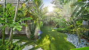 Un jardin luxuriant, agrémenté d’une variété de plantes tropicales, d’une pergola en bois et d’une pelouse bien entretenue.