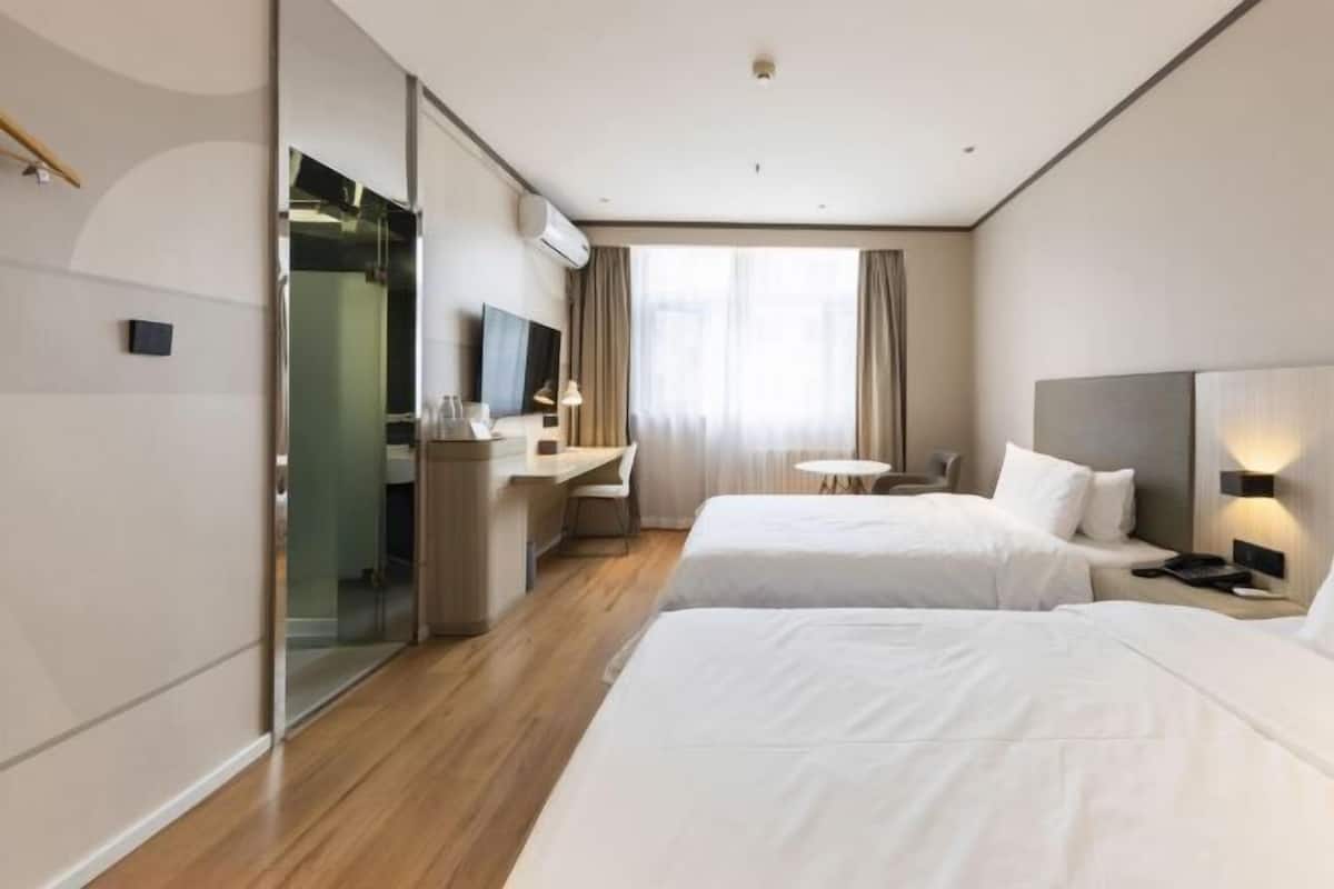 Une chambre d’hôtel avec deux lits, un bureau avec une chaise, une petite table ronde et un téléviseur.