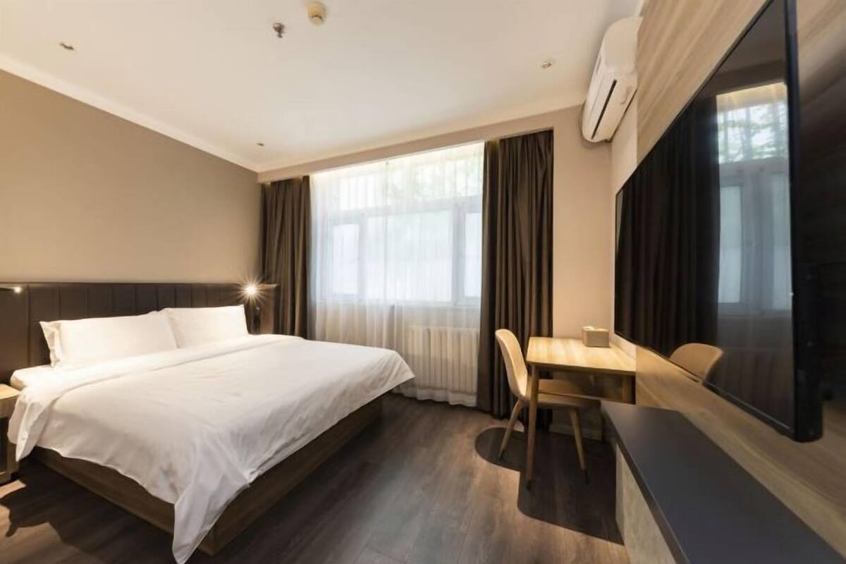 Une chambre d’hôtel équipée d’un lit, d’un bureau, d’une chaise, d’une grande fenêtre avec des rideaux et d’un appareil de climatisation.