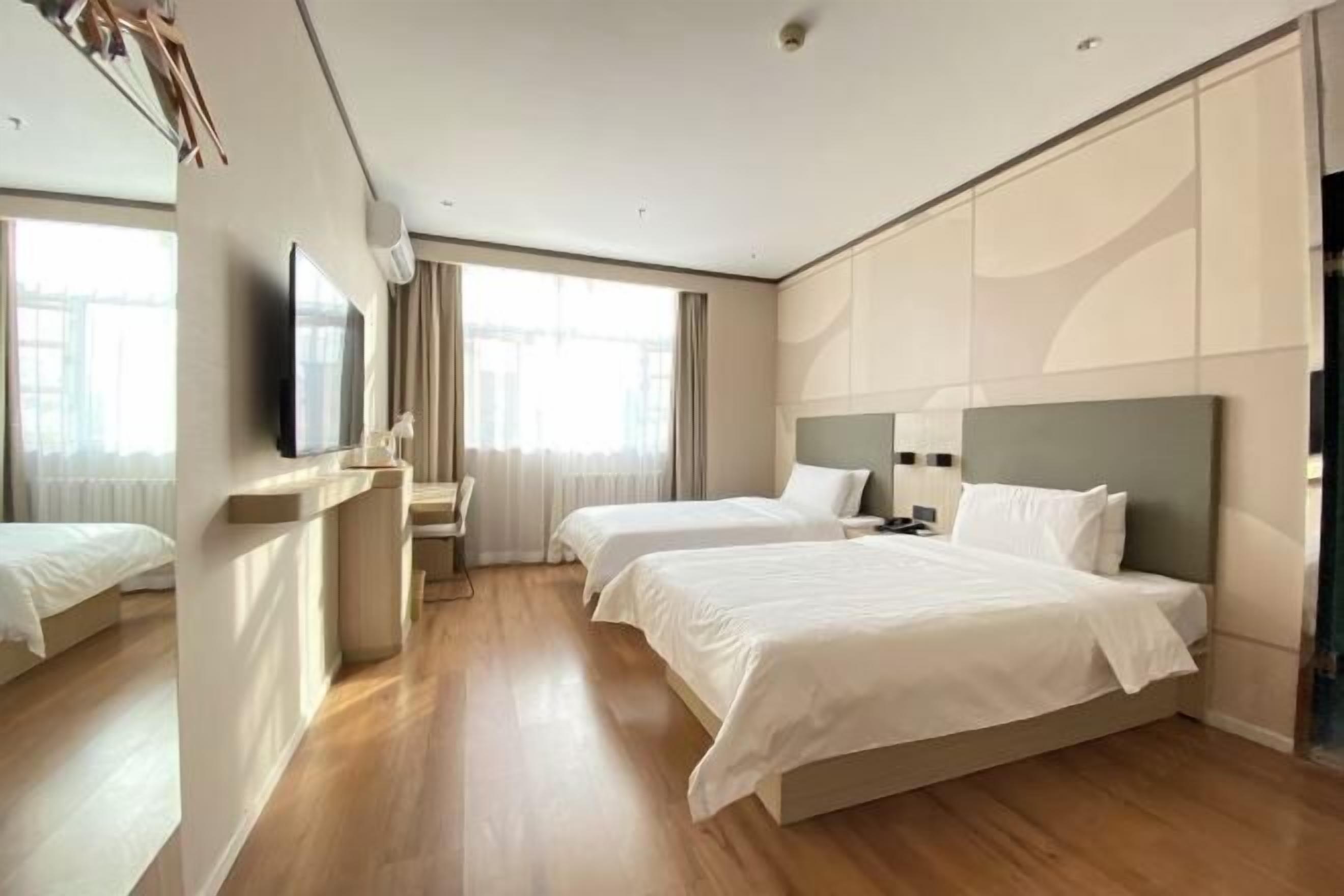 A hotel room with two beds, a TV, a desk, and a window with curtains.