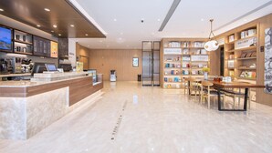 A modern hotel lobby with a reception desk, digital menu board, and a seating area with bookshelves. - Hanting Hotel (Zhengzhou)