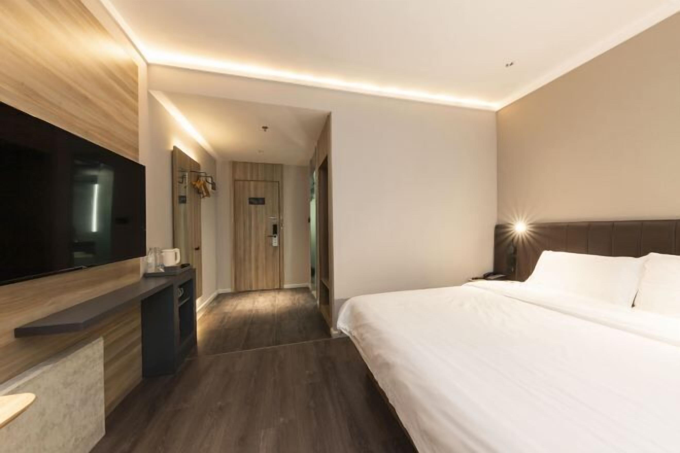 A modern hotel room with a large bed, a flat-screen TV, a desk, and a walk-in closet.