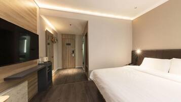 A modern hotel room with a large bed, a flat-screen TV, a desk, and a walk-in closet.