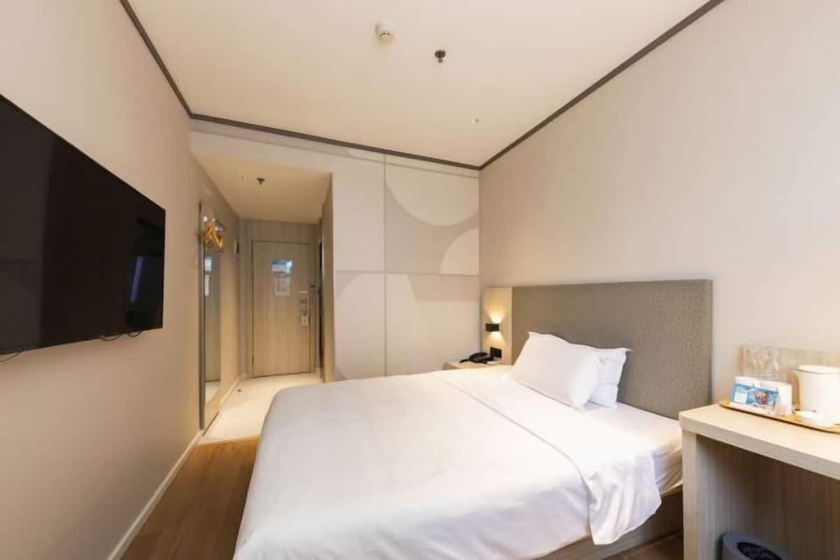 Une chambre d’hôtel moderne dotée d’un grand lit, d’un téléviseur à écran plat fixé au mur, d’une table de chevet avec une lampe et d’un petit bureau avec une machine à café.