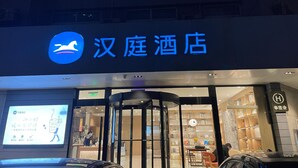 A hotel entrance with a sign reading '汉庭酒店' and a digital display board. - Hanting Hotel (Zhengzhou)