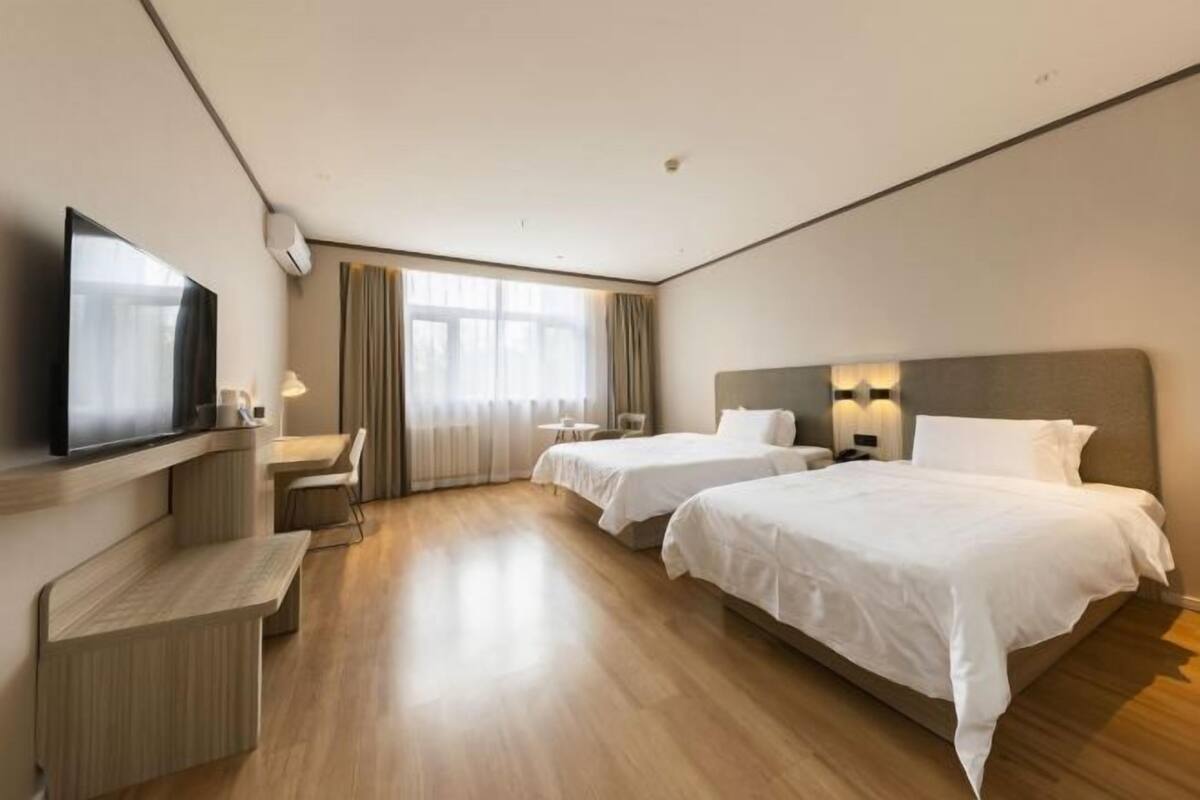 Une chambre d’hôtel avec deux lits, un bureau, une télévision et une grande fenêtre.