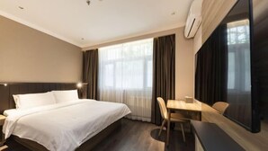 A hotel room with a large bed, a desk, and a chair. There is a window with curtains, a flat-screen TV, and an air conditioning unit on the wall. - Hanting Hotel (Zhengzhou)