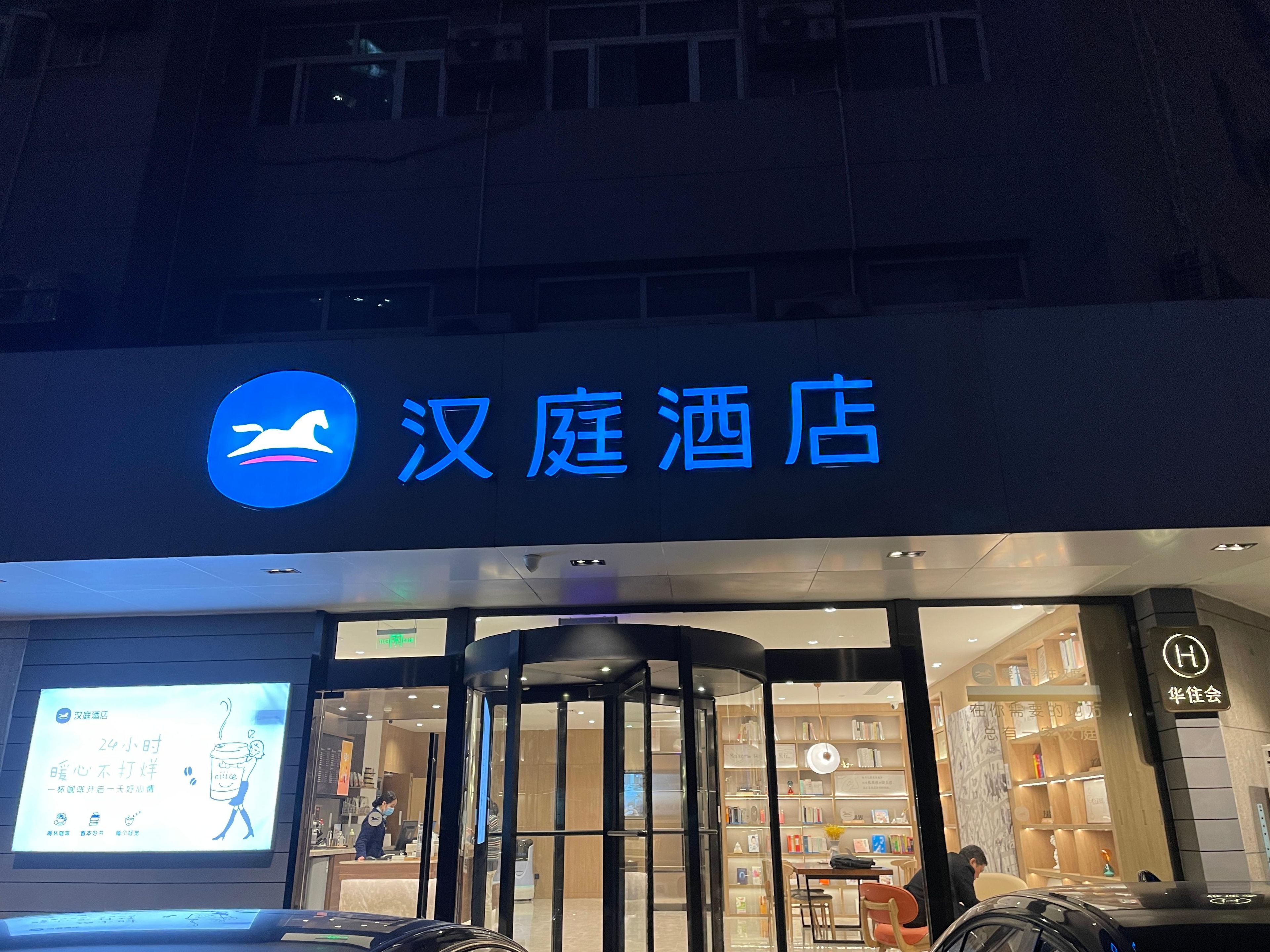 A hotel entrance with a sign reading '汉庭酒店' and a digital display board.